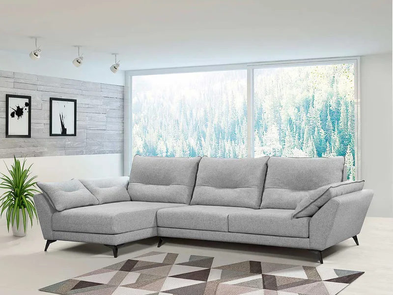 Sofá chaise longue gris de cuatro plazas con cojines, junto a un ventanal.
