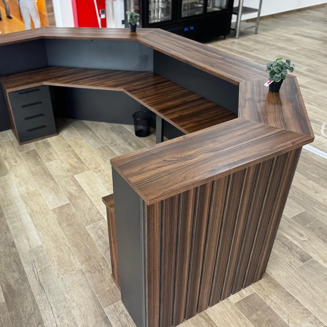 El mismo mostrador de recepción visto por detrás, con la encimera en nogal y el office en ele con cajonera.